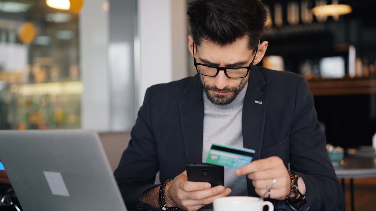 A man in glasses holding a credit card and looking at his phone